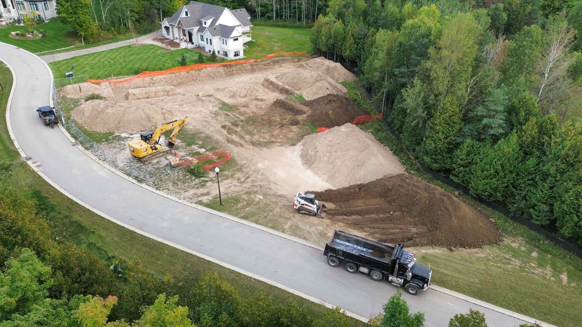 Country Estates Construction excavation: aerial drone view of an excavator and dump truck on a lot beside a road