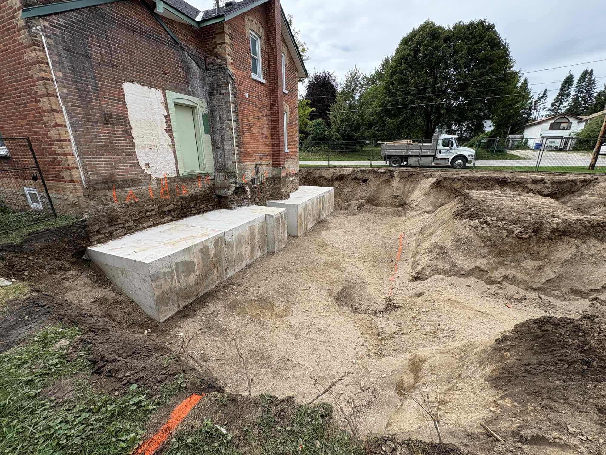 Country Estates Construction excavation: excavation beside an old brick house, with new concrete footings along the foundation wall