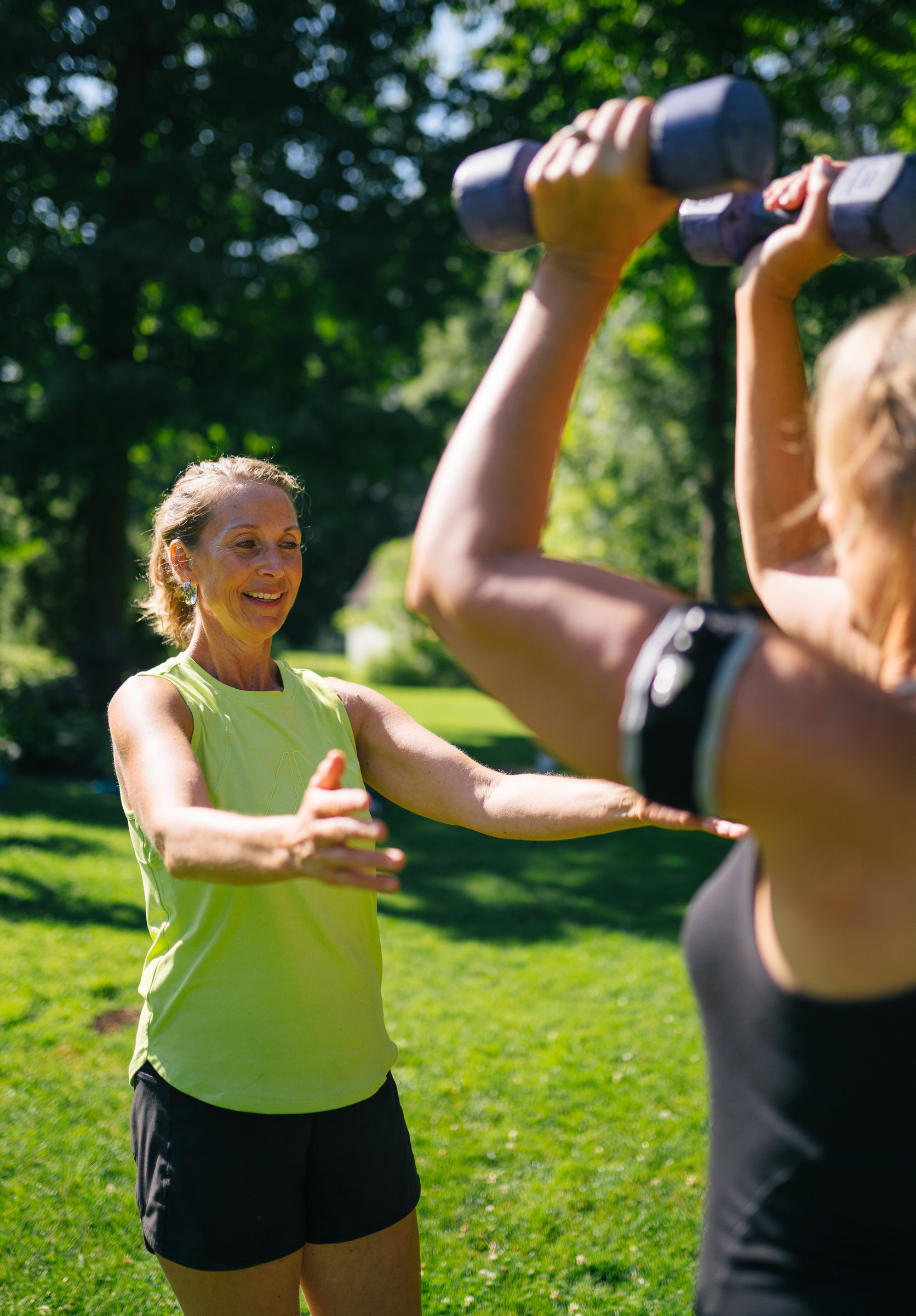Kaley coaching a client who lifts dumbbells with a BFR band on her arm