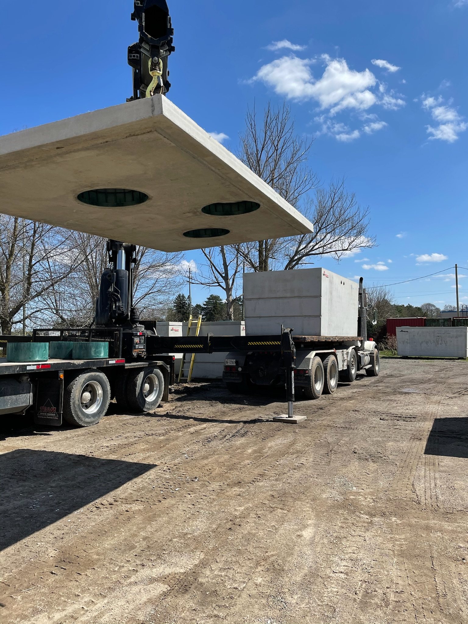 Crane truck lowering a concrete septic tank lid into place