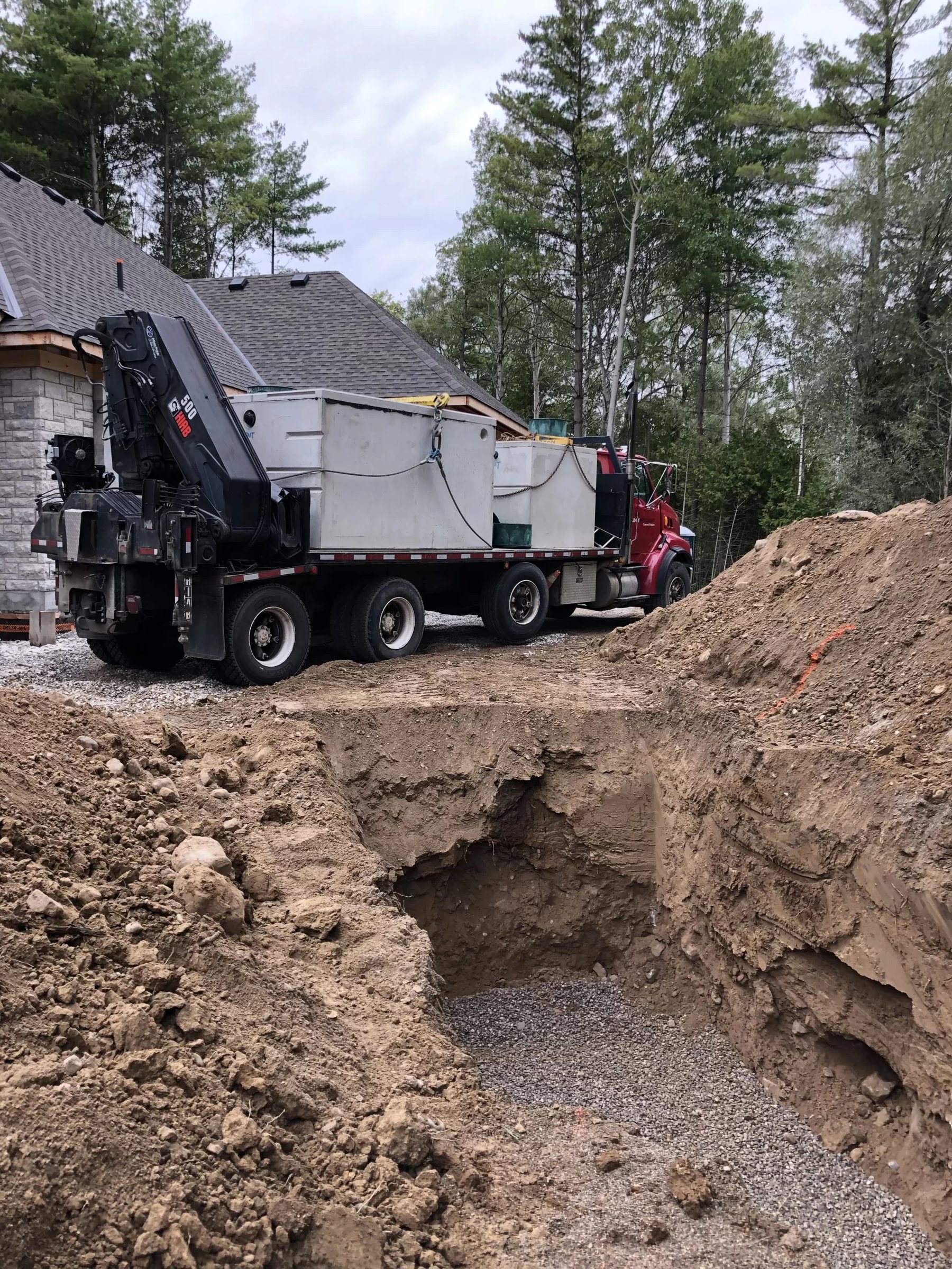 Crane truck unloading a tank beside a deep excavation