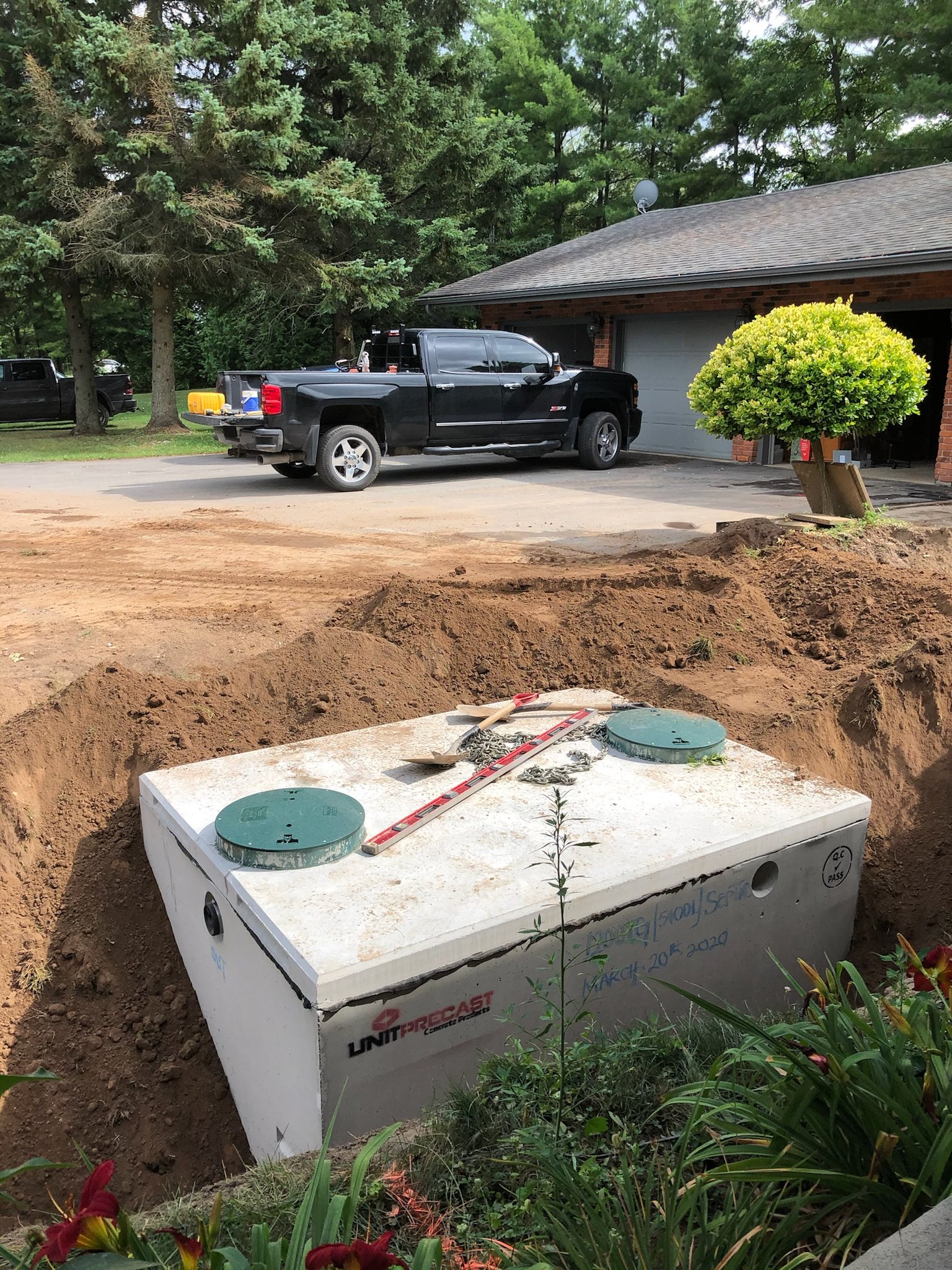 Concrete septic tank set in the ground beside a driveway, ready for backfill
