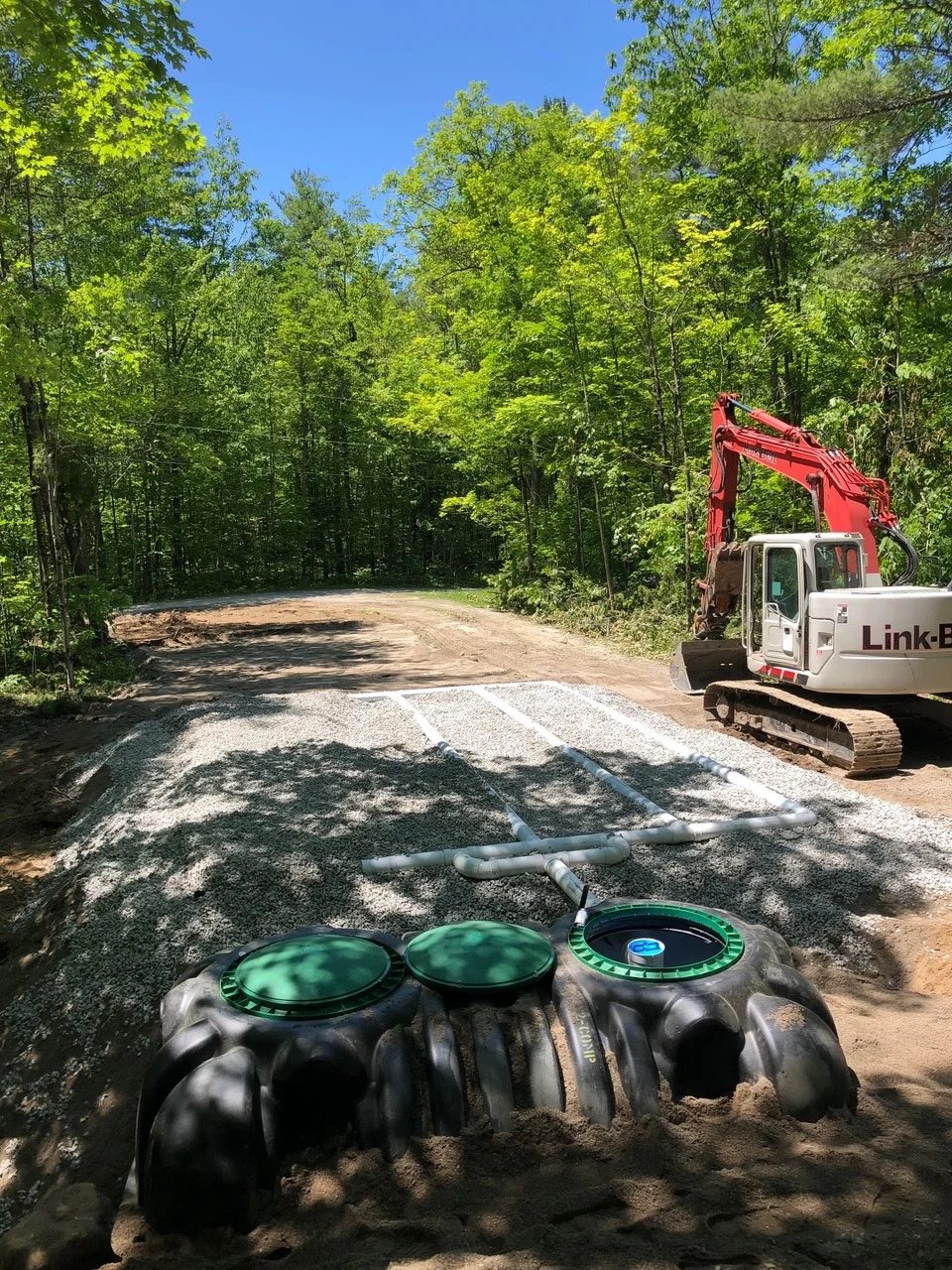 Septic tanks with green access lids set on stone in a wooded lot
