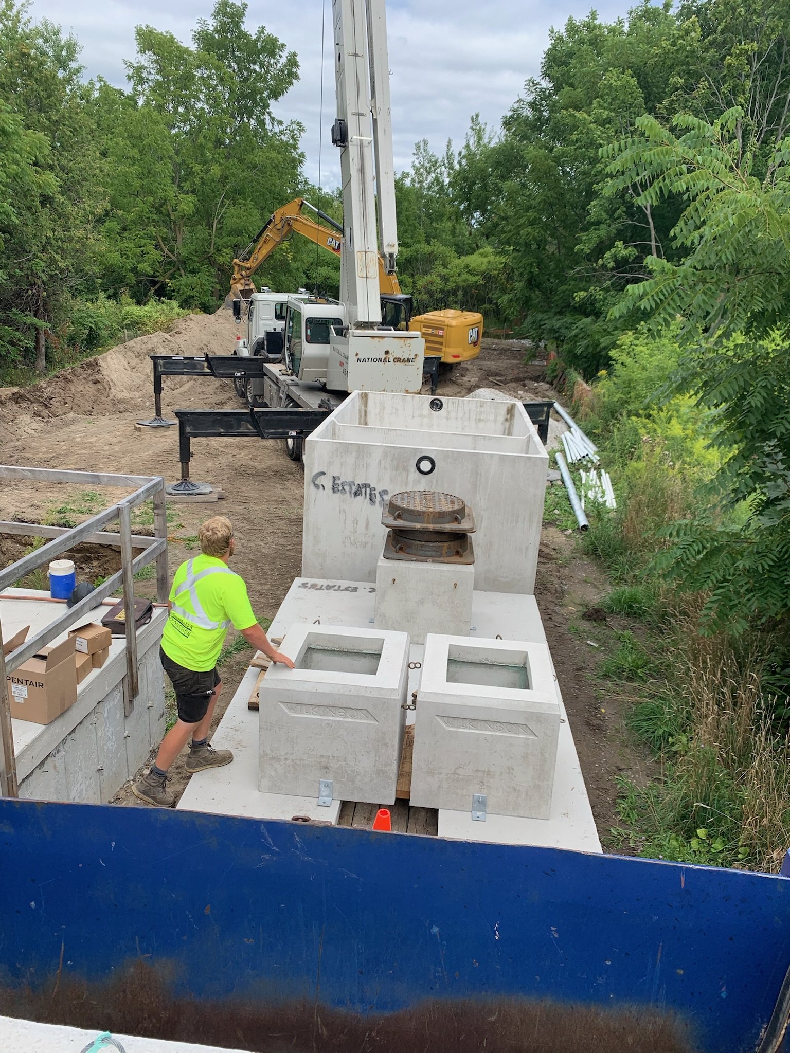 Concrete tank being set in a trench by crane beside a house