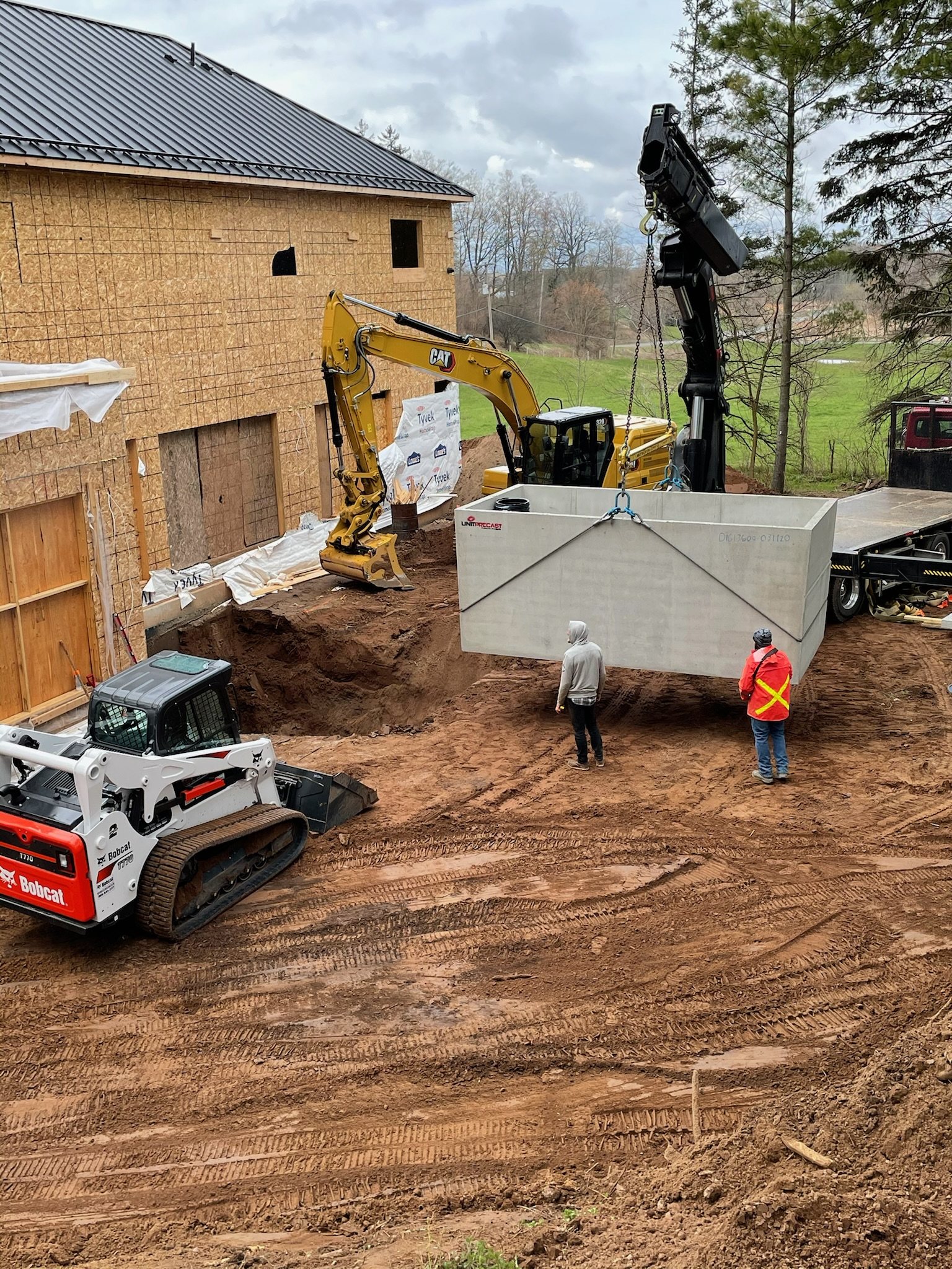 Country Estates Construction septic installation: crane carrying a concrete septic tank across a new home build site