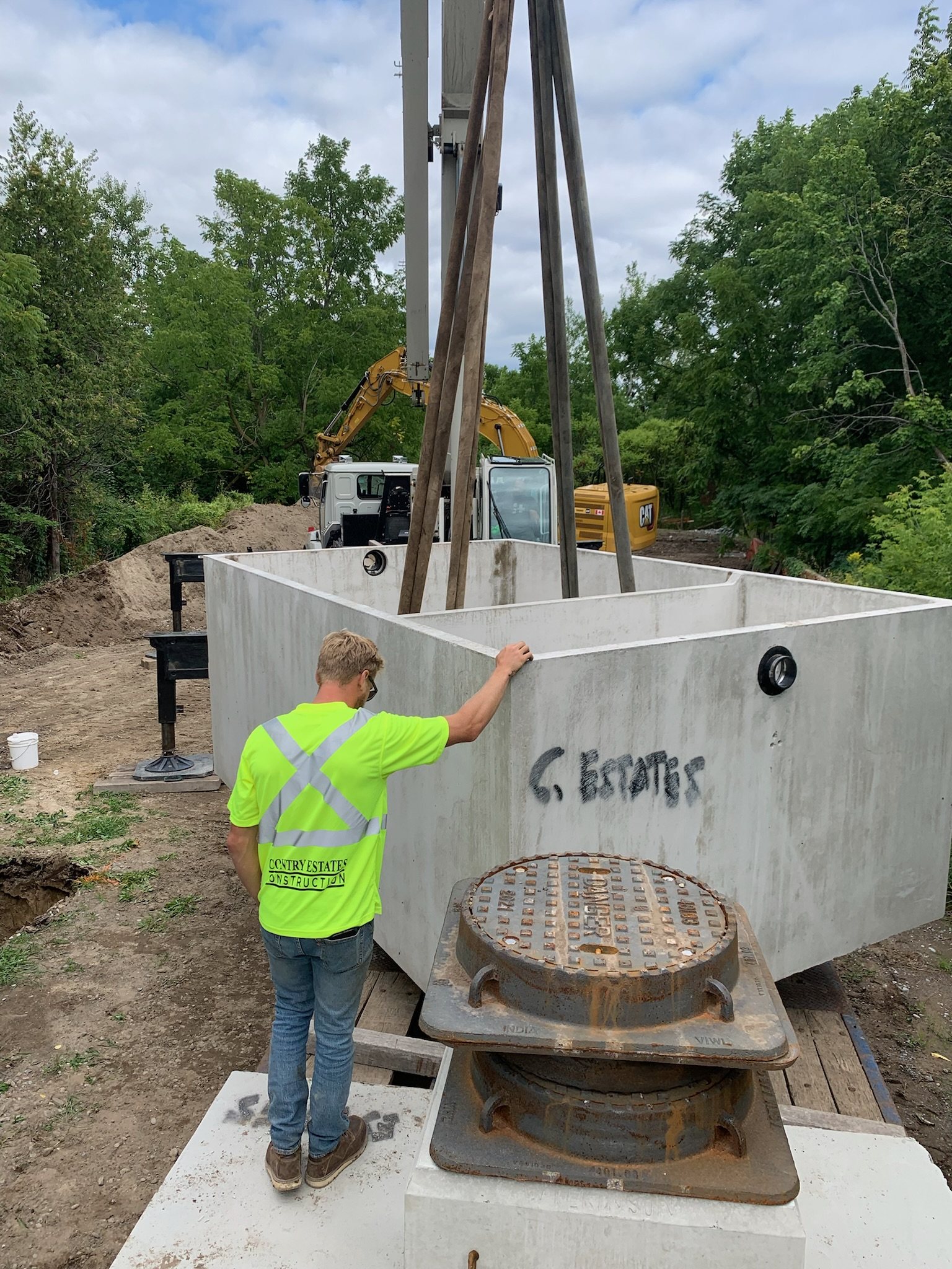 Crew member guiding a Country Estates septic tank as a crane sets it